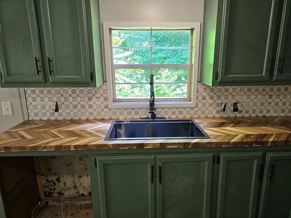 Front view of a black sink, herringbone wood counters and green cabinets