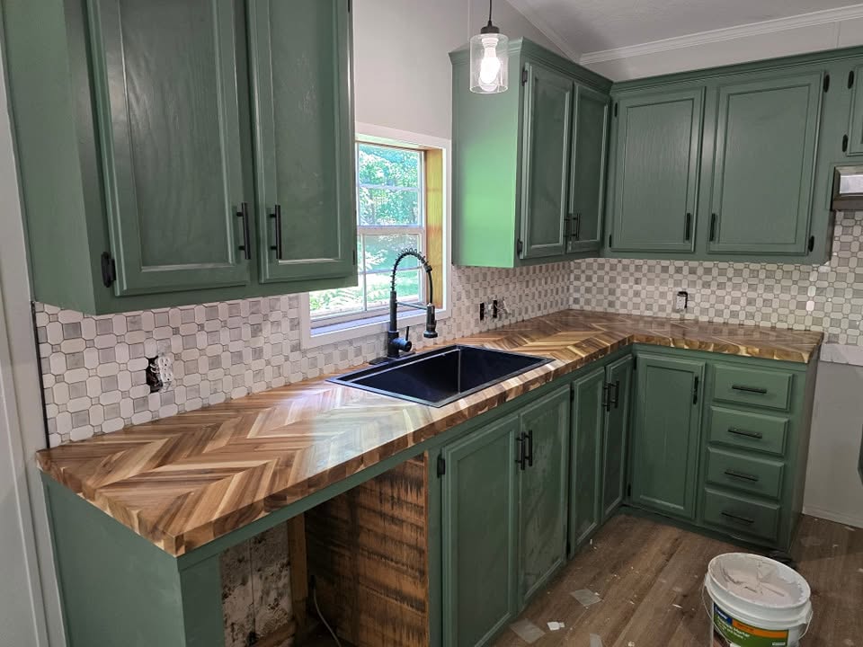 Green kitchen cabinets with herringbone wood counters and tile backsplash