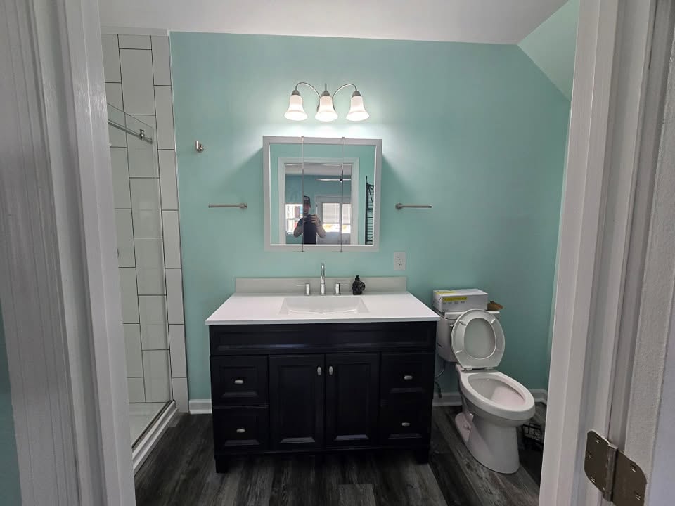Dark bathroom vanity with white counter and mirror against a pale blue wall