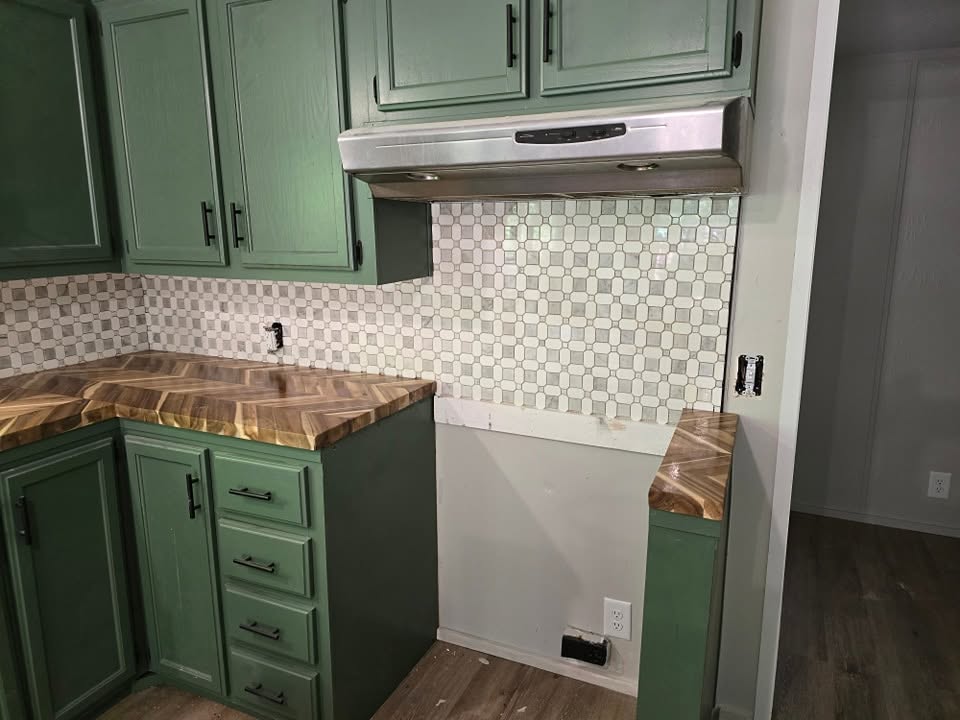 Green shaker cabinets with herringbone butcher-block counters, tile backsplash and an under-cabinet range hood