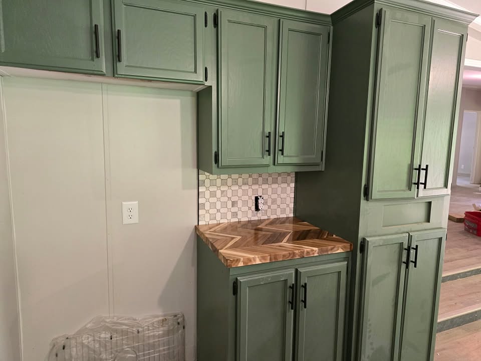 Tall green pantry cabinets and herringbone butcher-block counters beside a refrigerator alcove